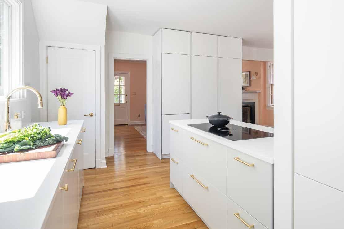 White kitchen with brass handles, an island hob and a vase of tulips