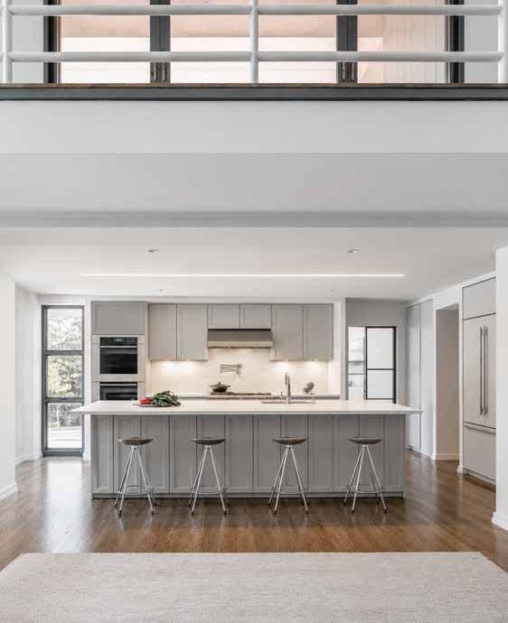 Long kitchen with a grey island and stools, seen from under a glass balcony