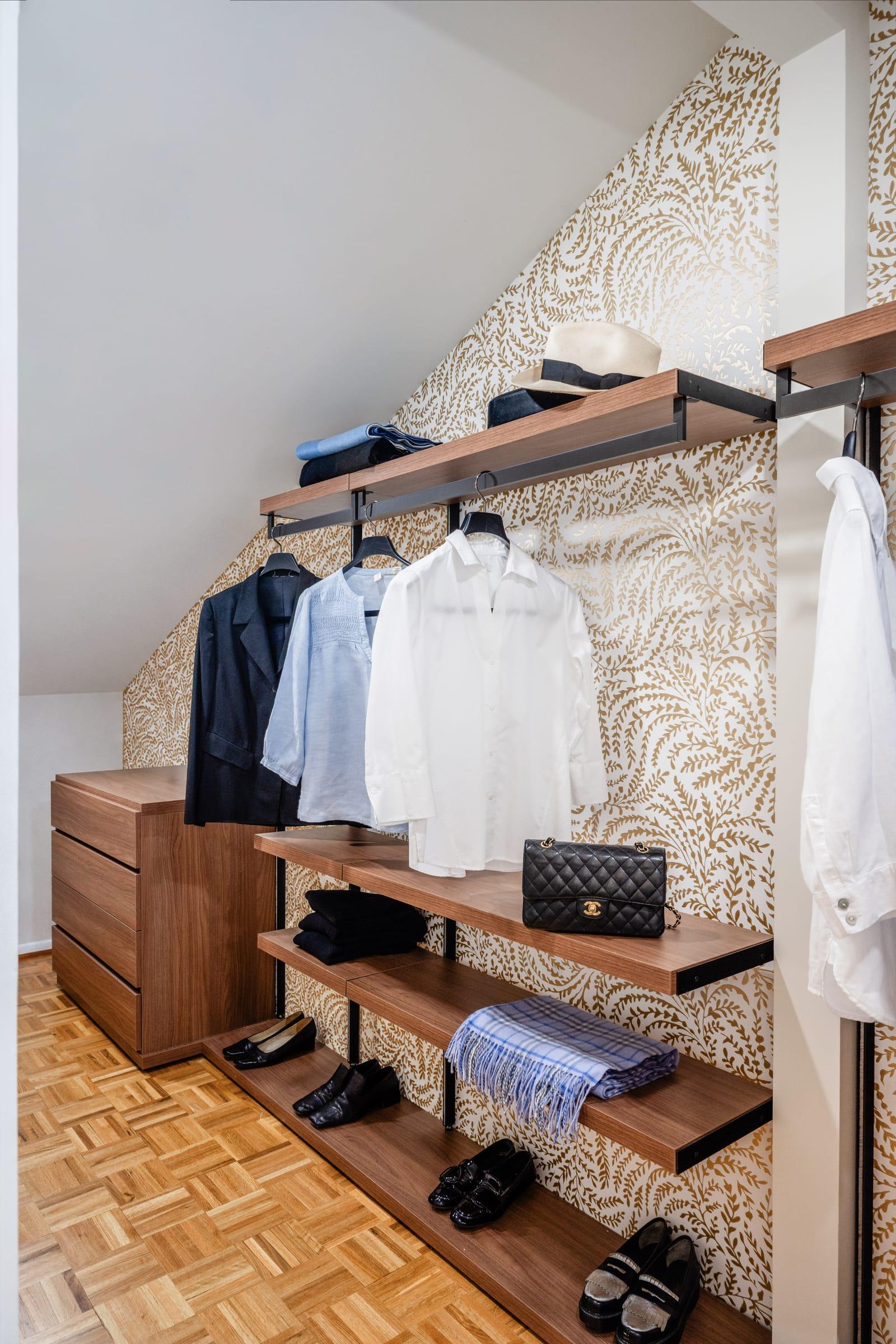 Open walnut wardrobe with shirts and shoes against a patterned wallpaper