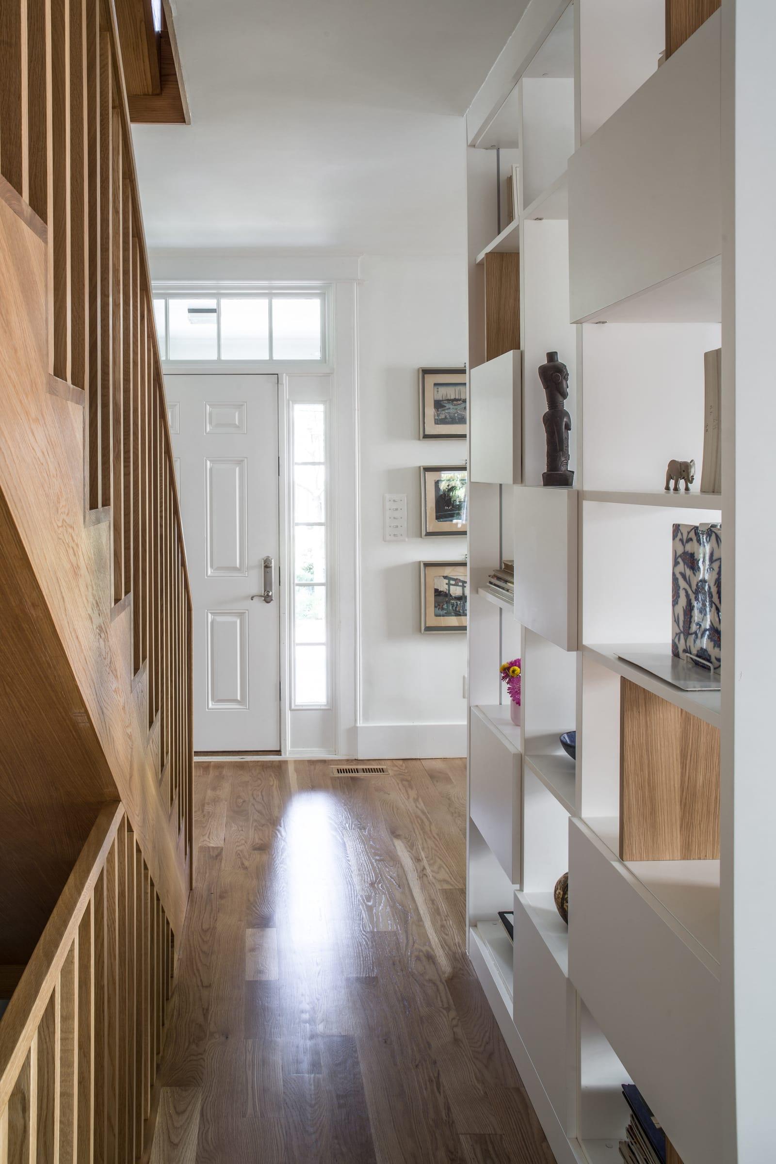 Hall with an oak staircase beside the white bookcase, the front door at the end