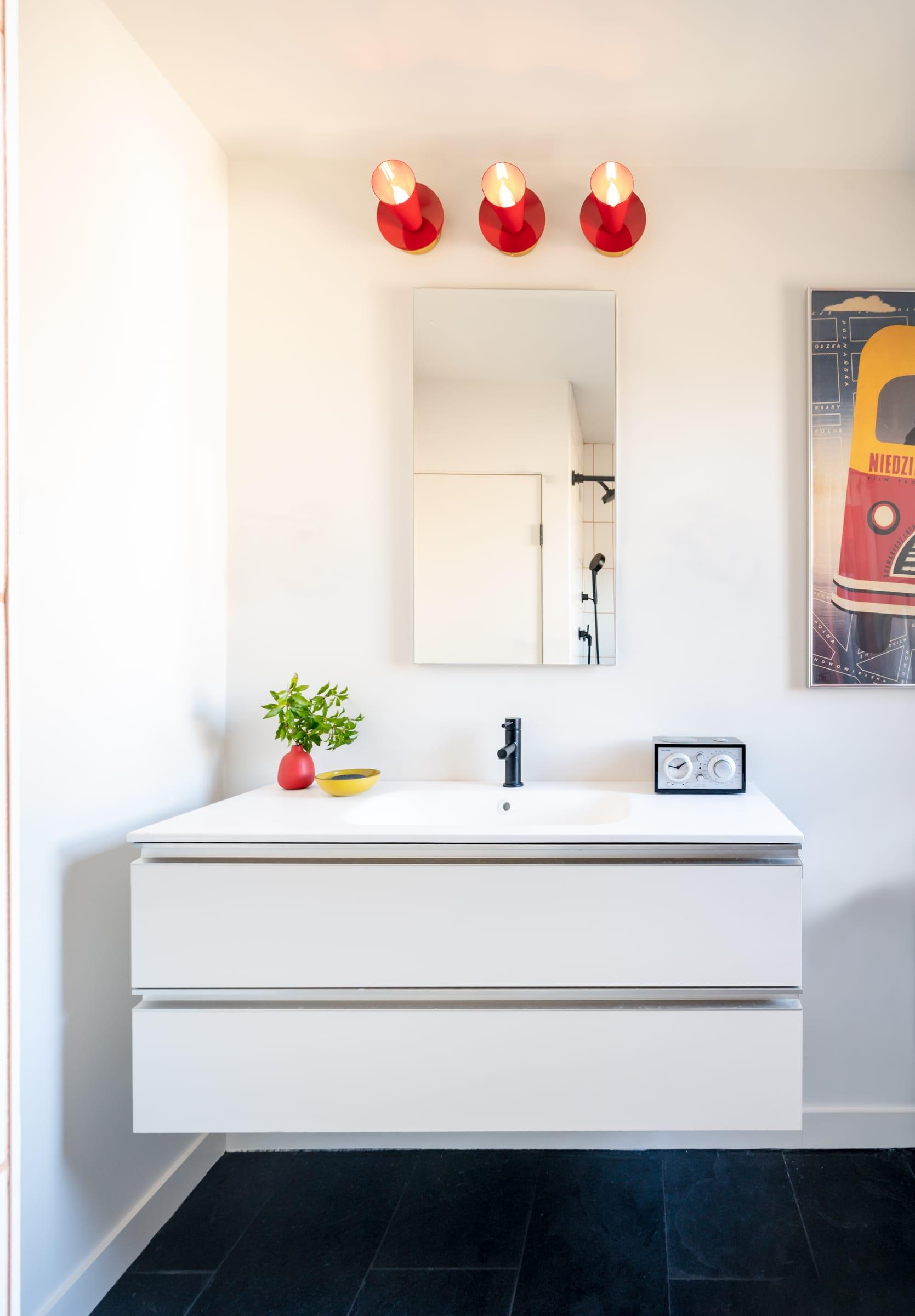 White vanity under a mirror and red wall lights