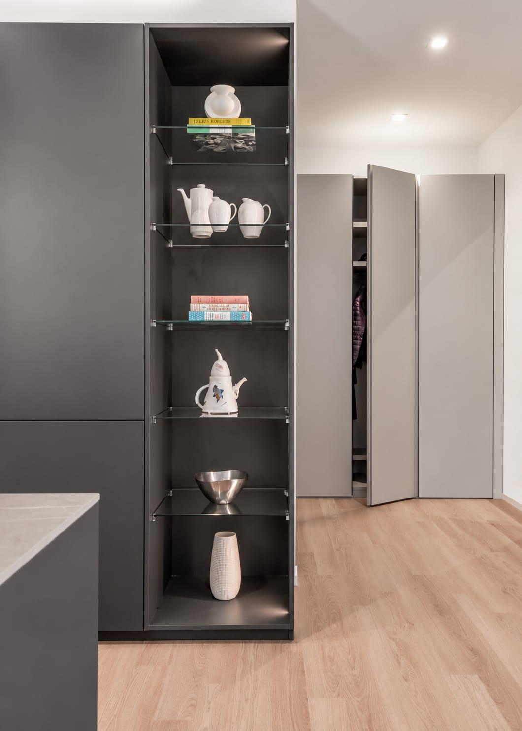 Black tall unit with lit glass shelves beside a grey wardrobe