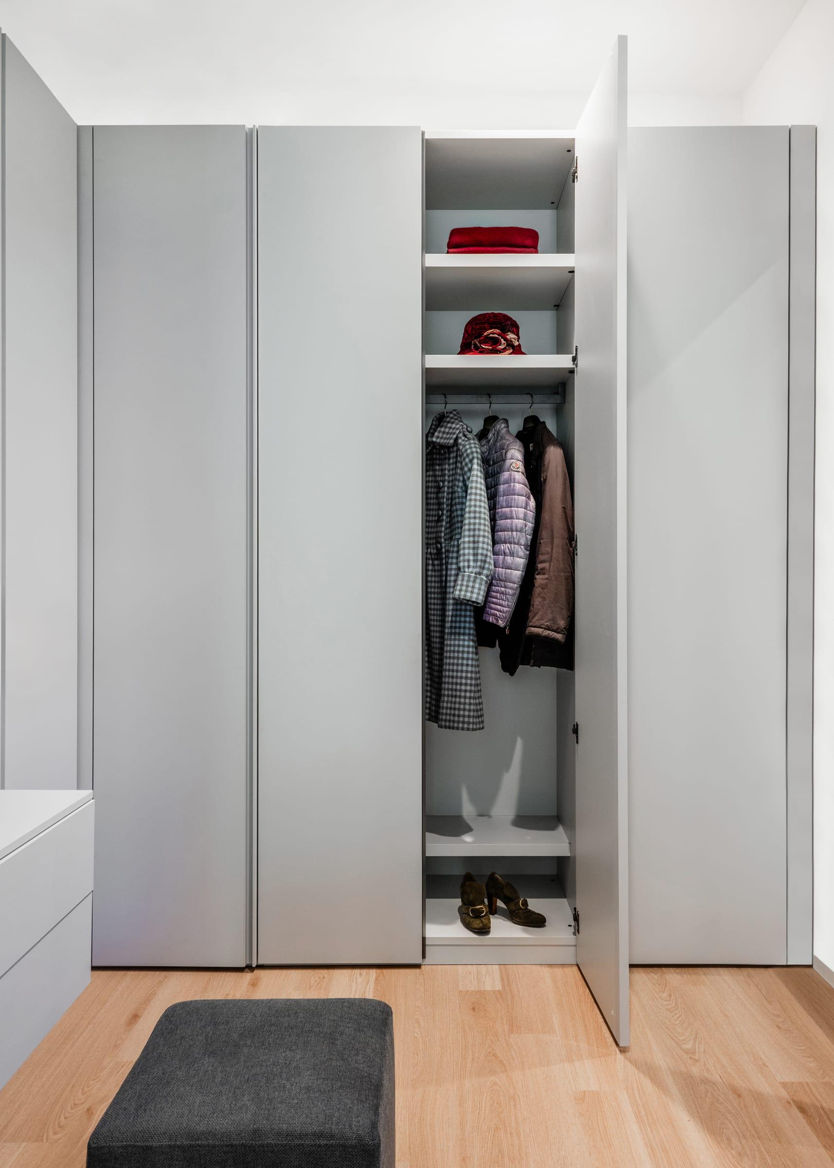 Grey wardrobe open onto hanging coats, a stool in front