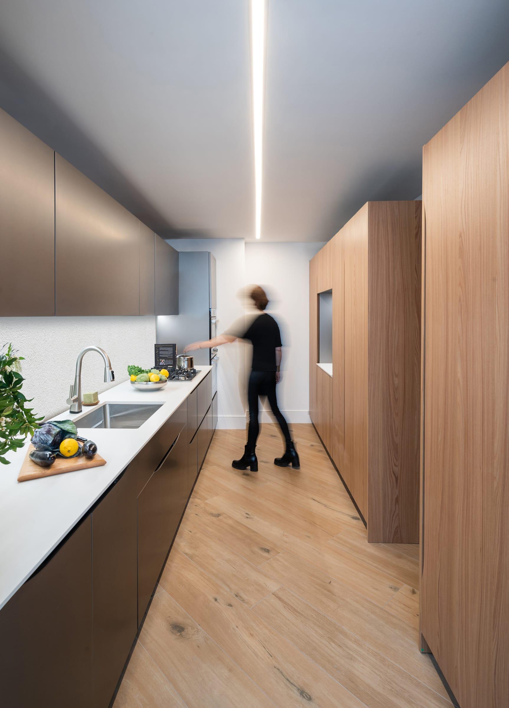Galley kitchen in wood and grey with a figure walking through