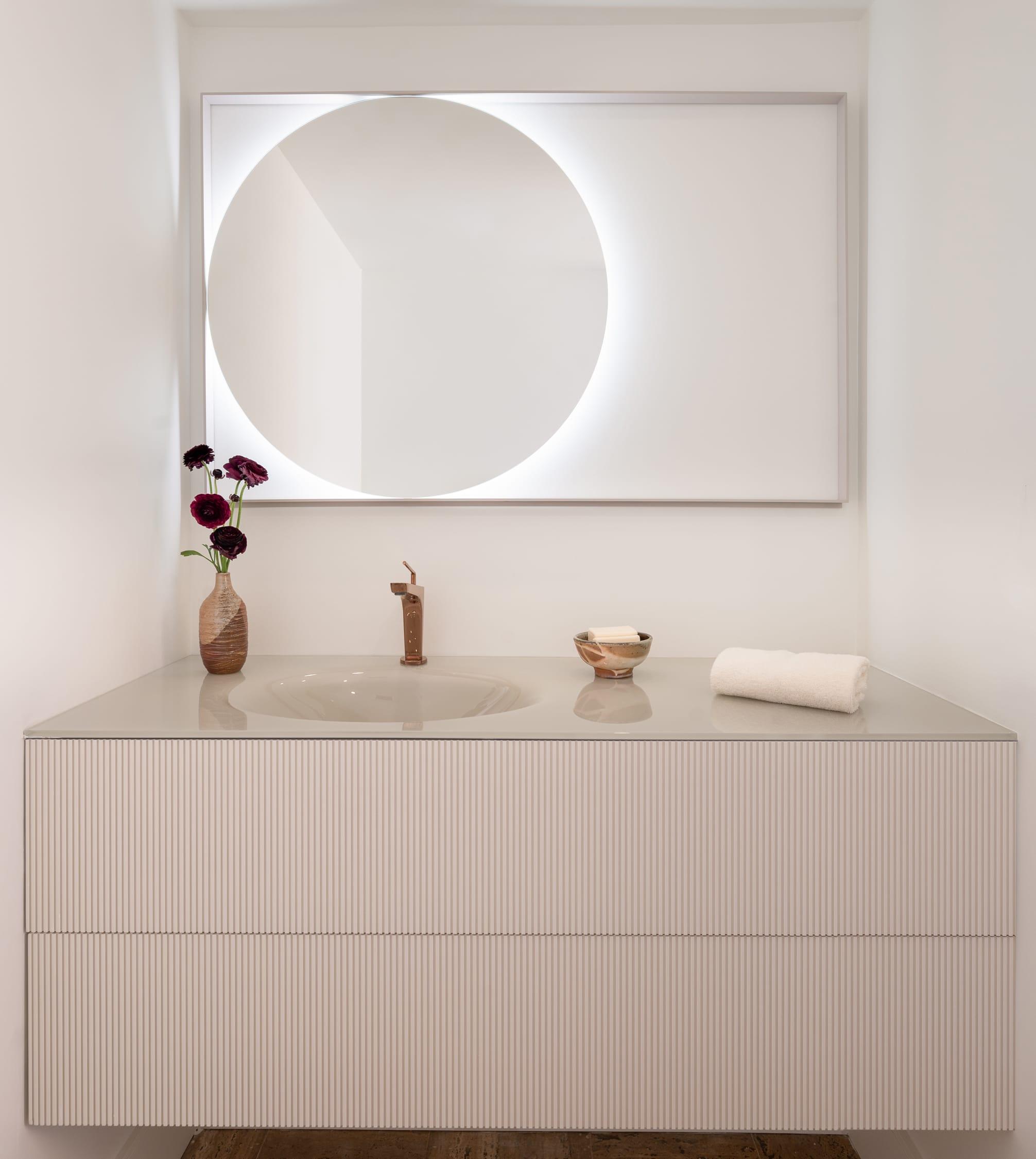 Pale vanity under a round lit mirror