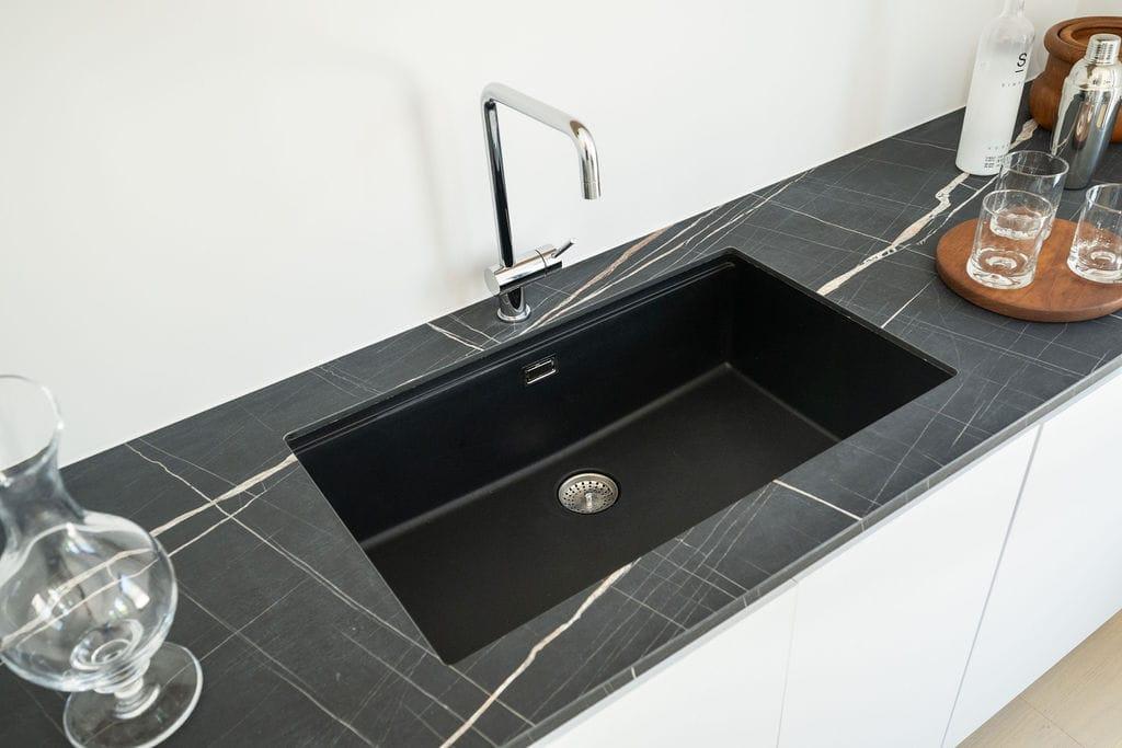 Black sink in a marble worktop with glasses