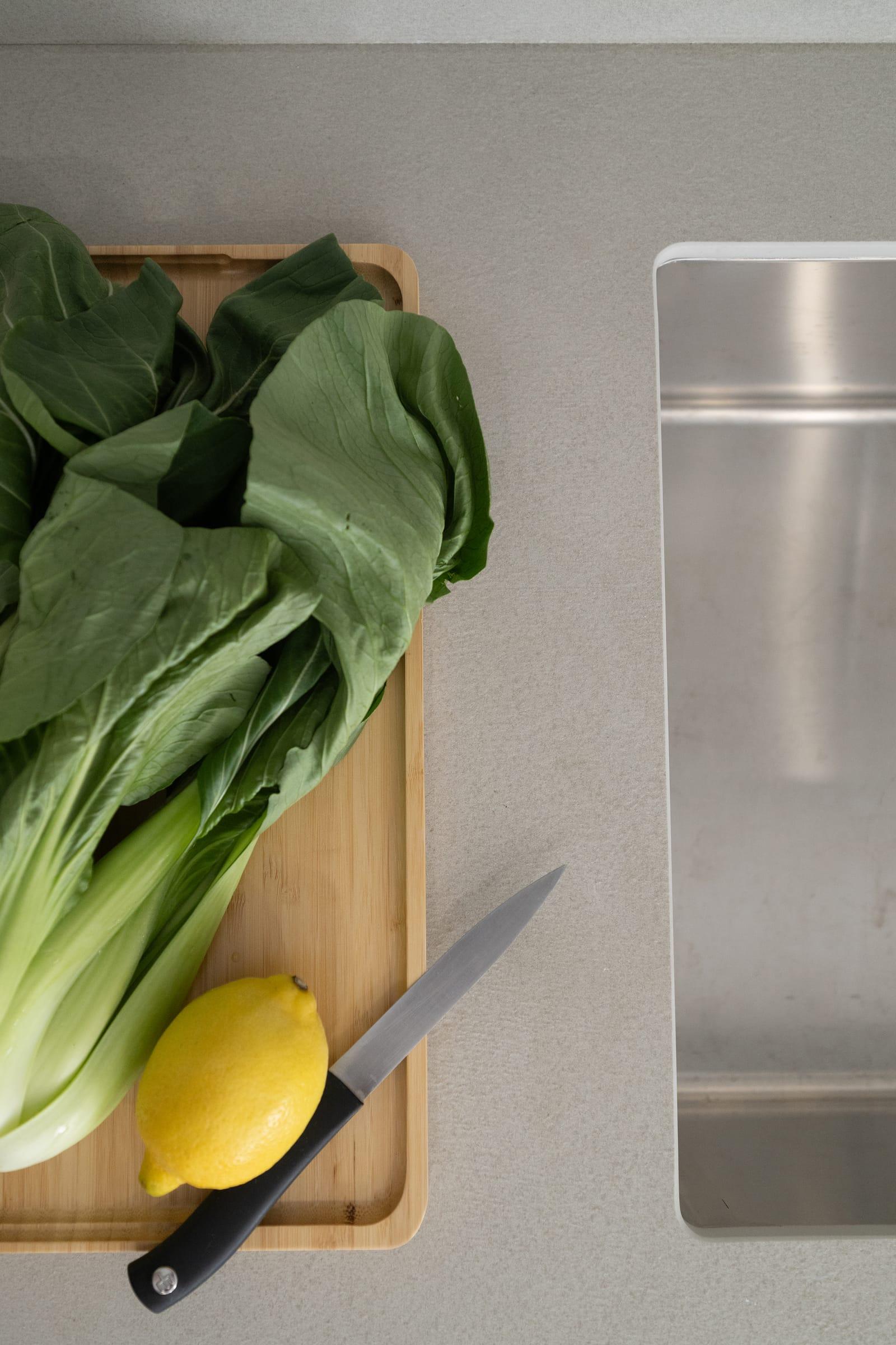 Chopping board with greens and a lemon beside a sink