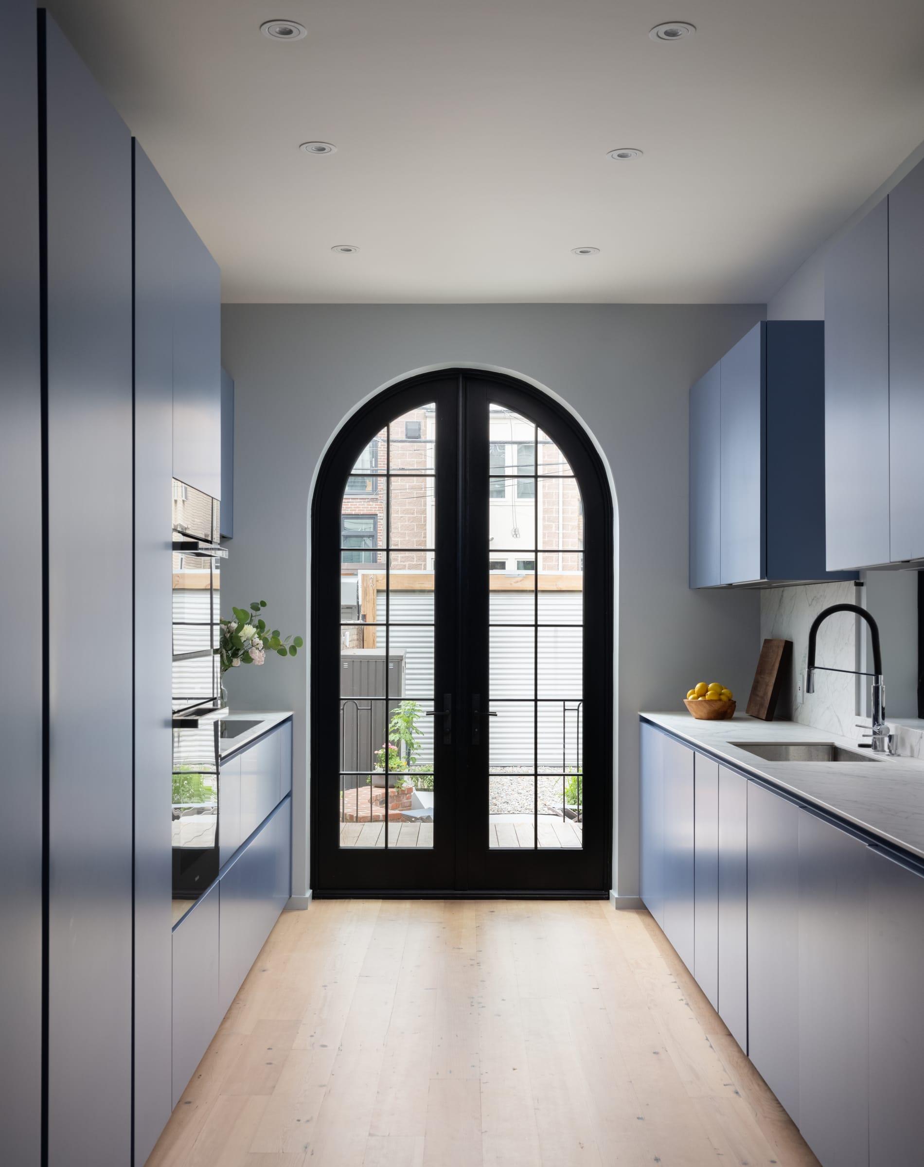 Blue galley kitchen leading to an arched glazed door