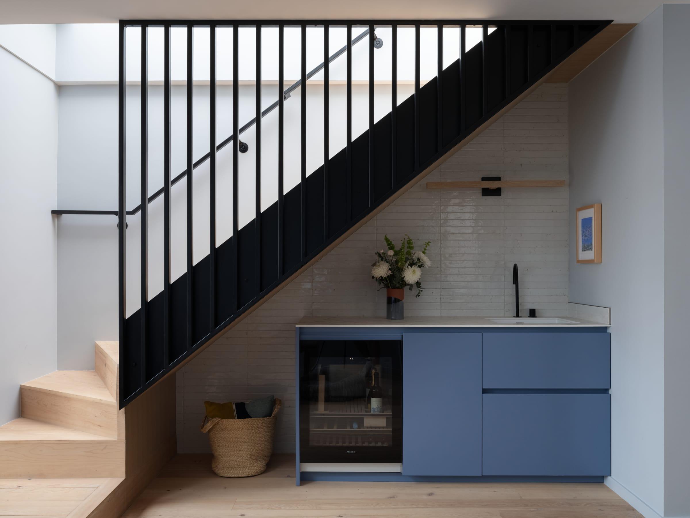 Blue cabinet with a wine fridge under a black staircase