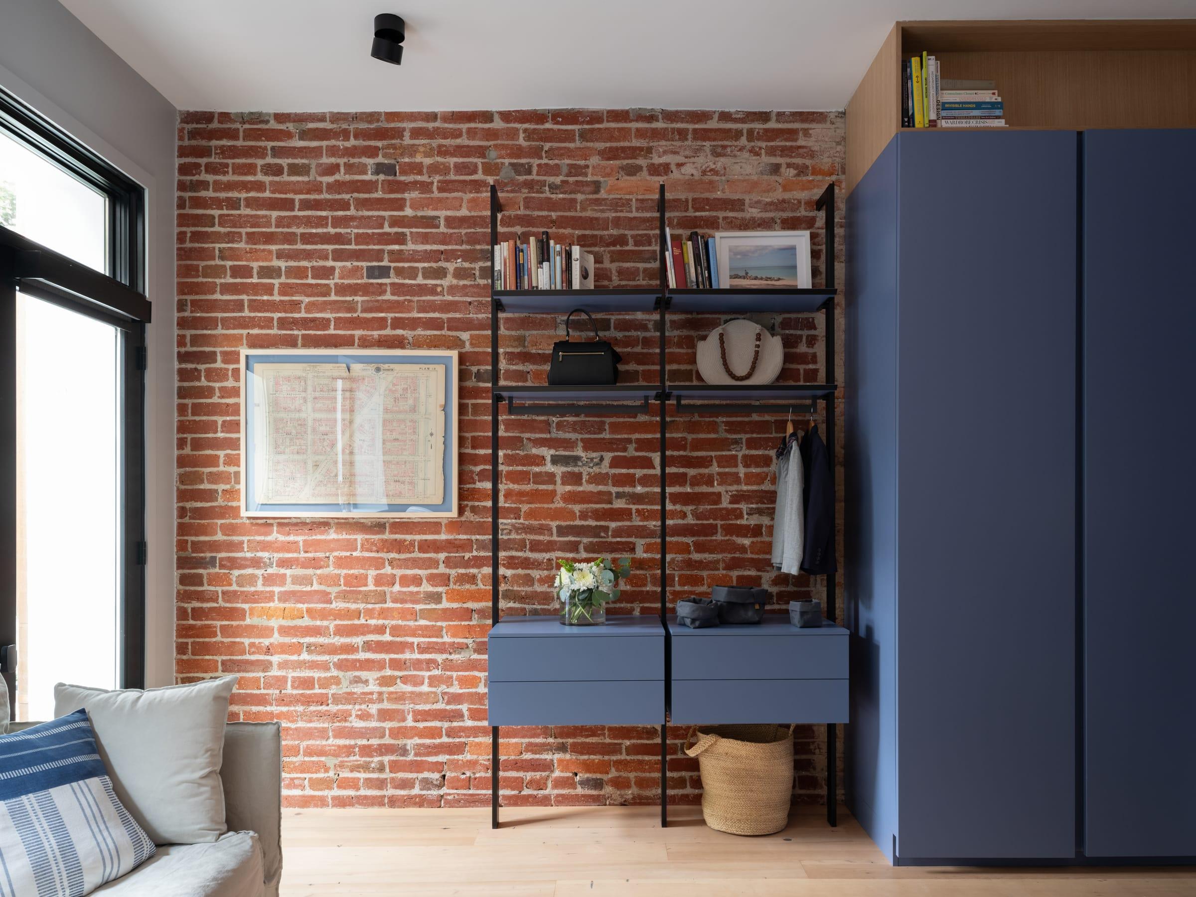 Brick-walled living room with a blue wardrobe and a wall-hung desk with shelves