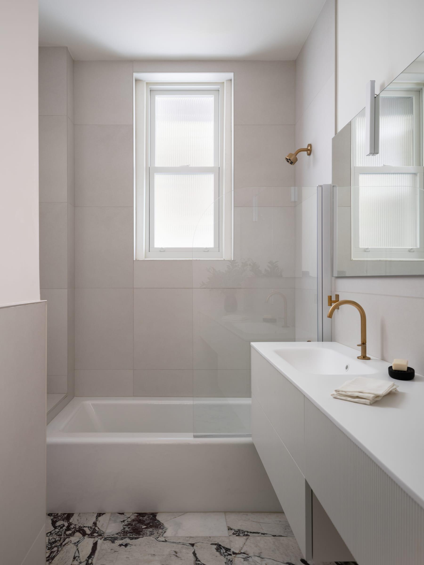 White bathroom with a tub, a long vanity and a marble floor