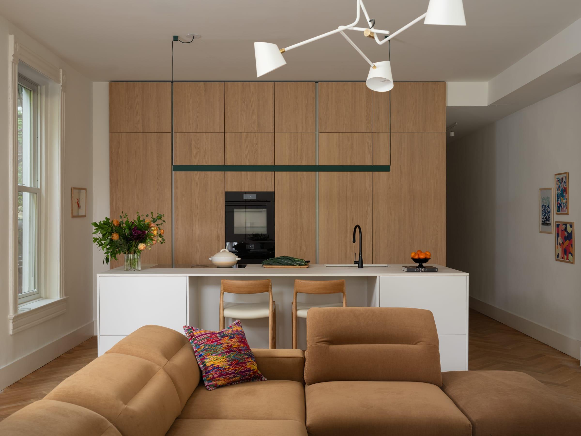 Oak wall of tall units behind a white island, a sofa in front