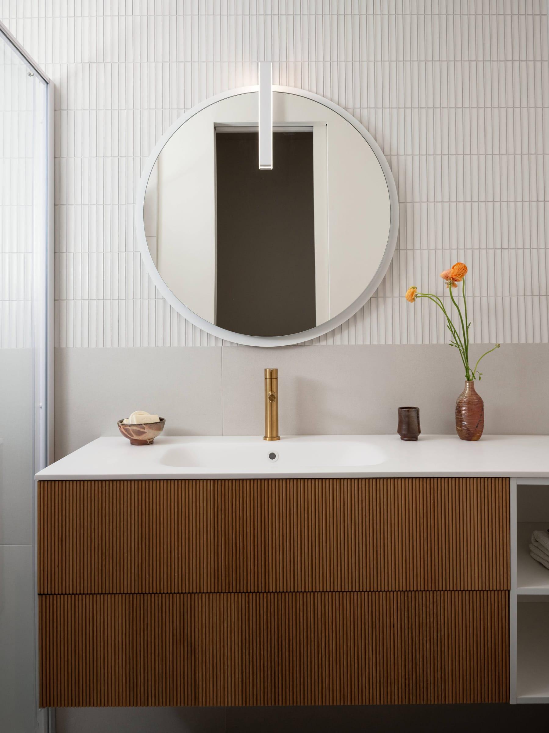 Walnut vanity with a white basin under a round mirror