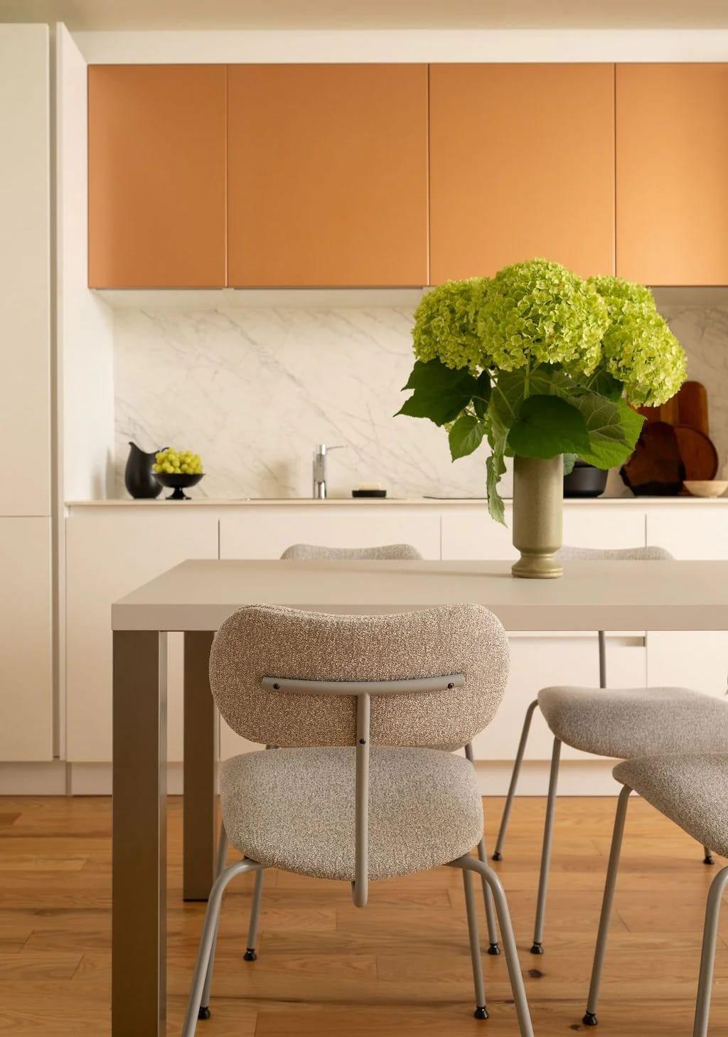 Dining table with upholstered chairs under copper wall cabinets and a vase of hydrangeas