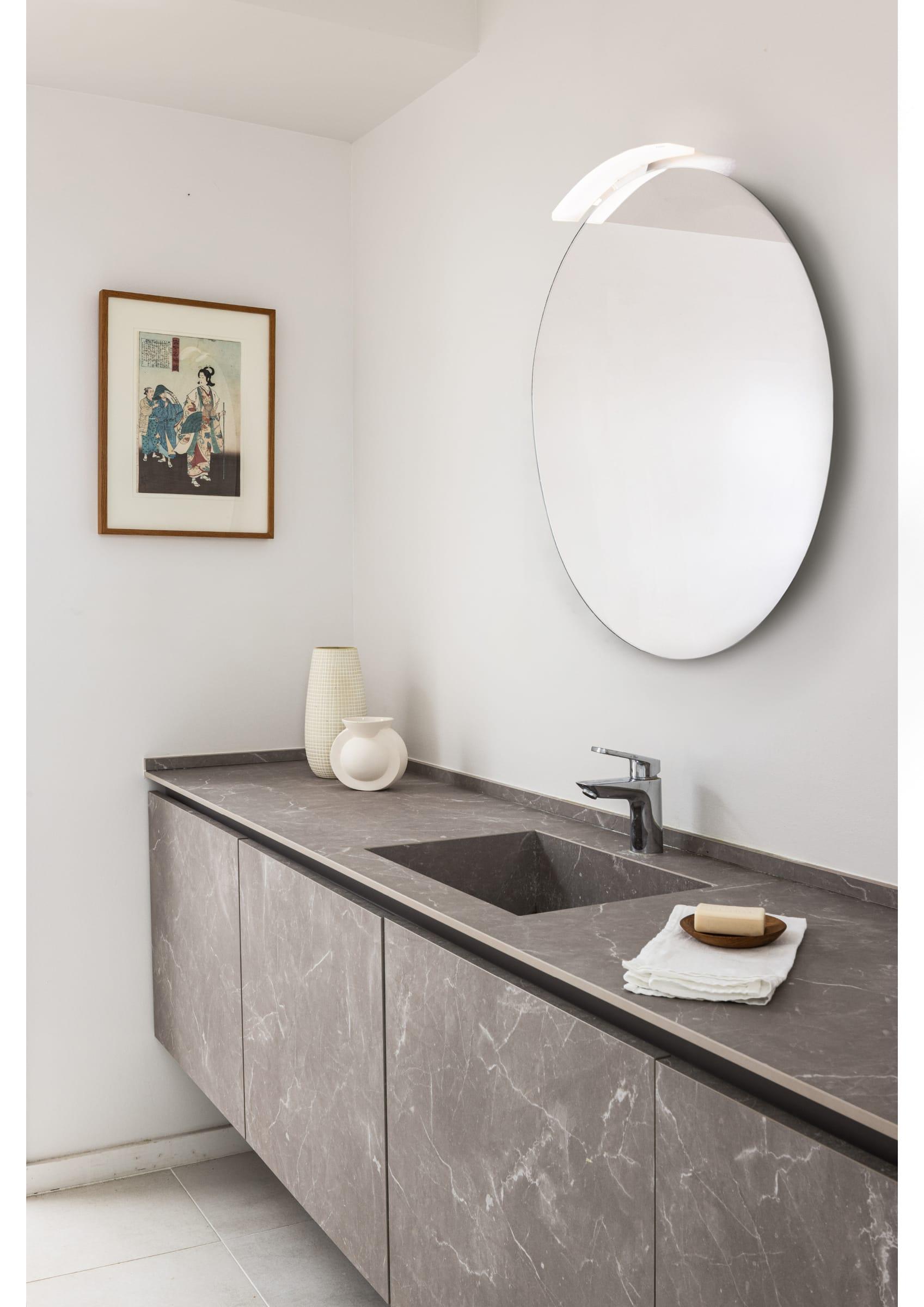 Grey stone vanity under a round mirror and a framed print