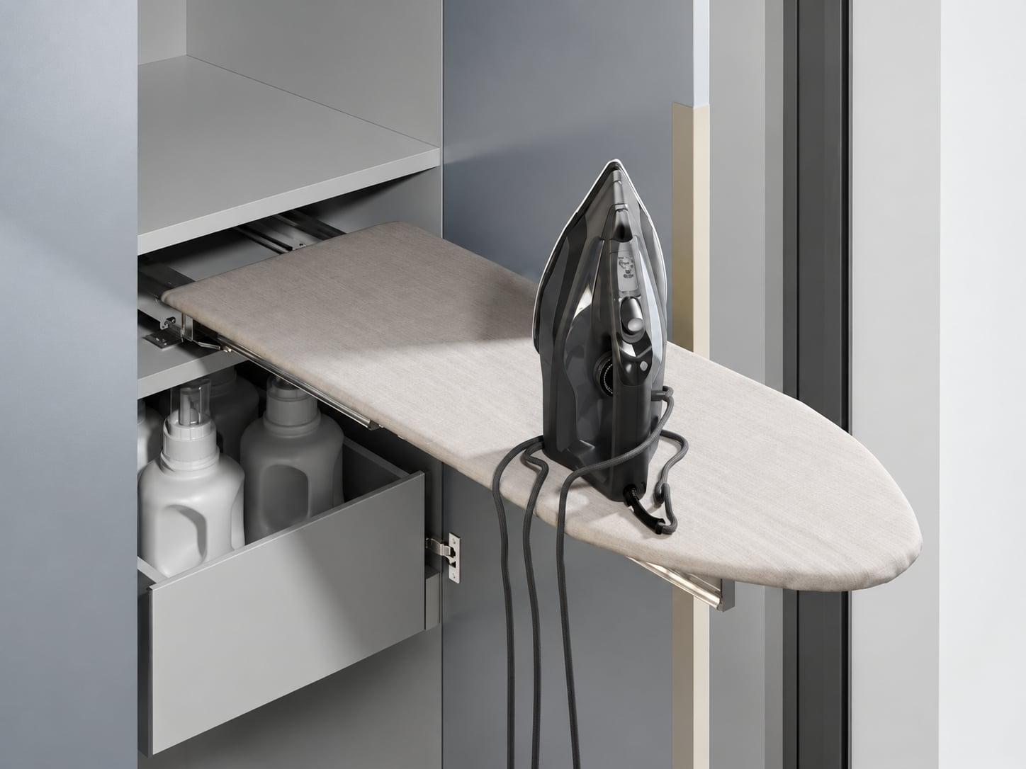 Ironing board folding out of a cabinet above a drawer of detergents