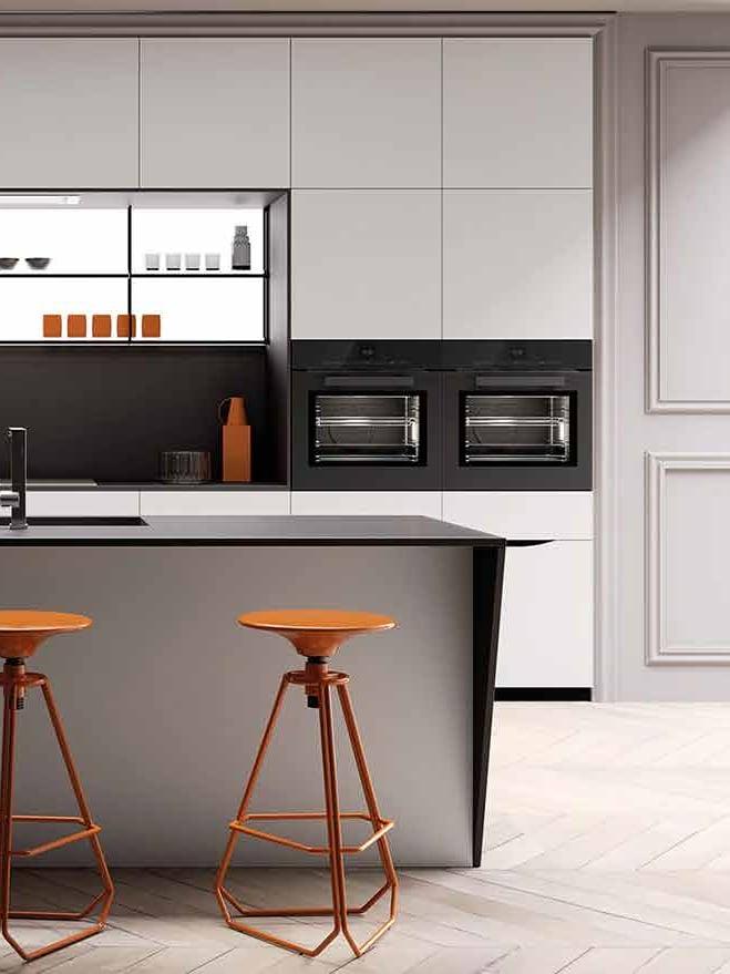 Kitchen island in grey with three orange metal stools, white handleless wall units and a backlit shelf niche