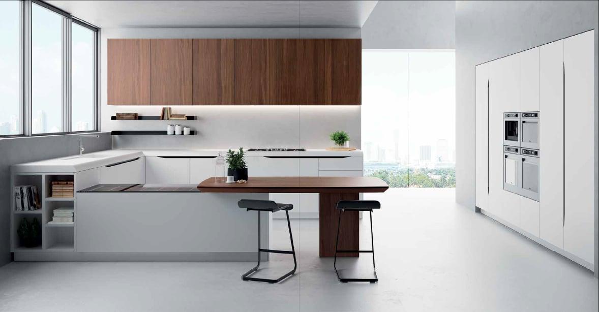 White kitchen with a walnut wall unit over an island that runs into a dining table, black bar stools beside it