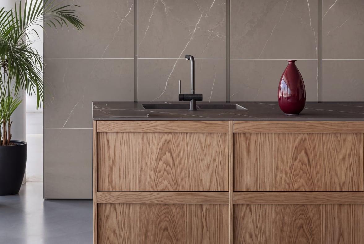Kitchen island in oak with a black tap in front of a dark marble wall