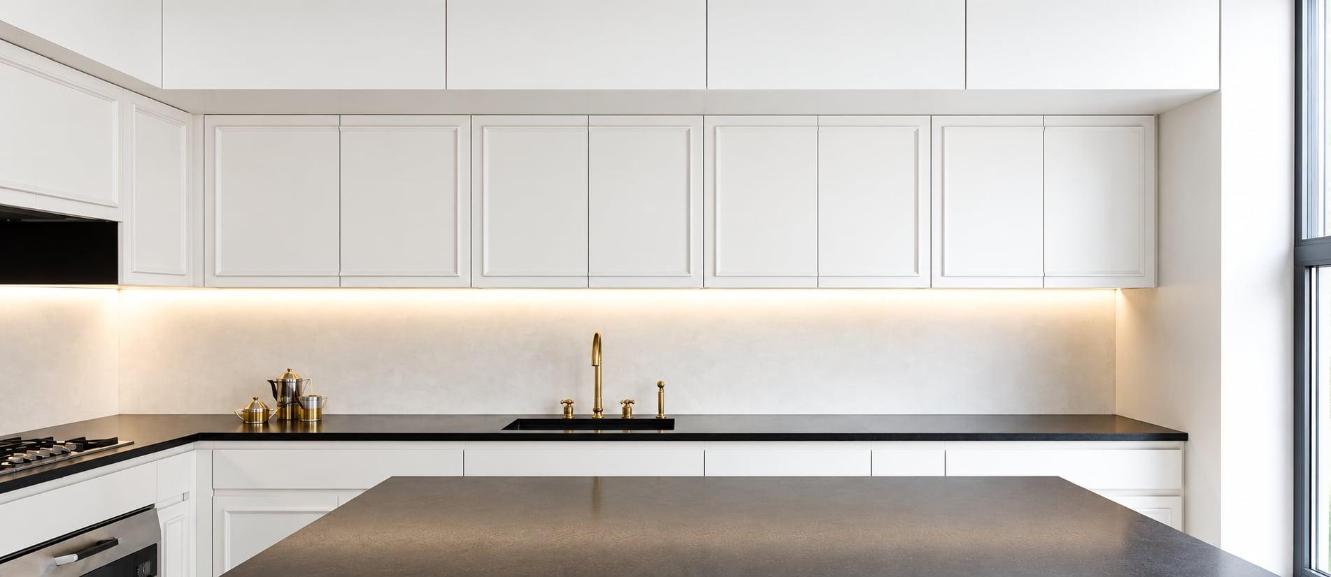 White panelled kitchen with brass taps, under-cabinet lighting and glass pendants over the island