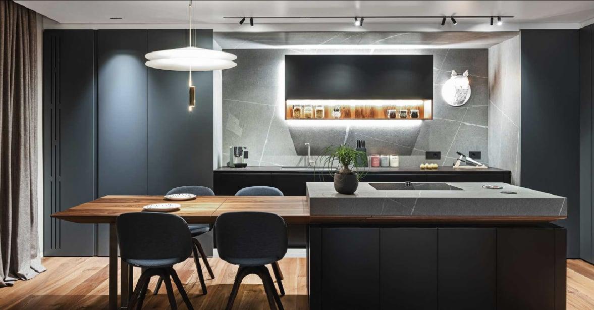 Dark kitchen with a wood dining table extending from the island, under a white pendant