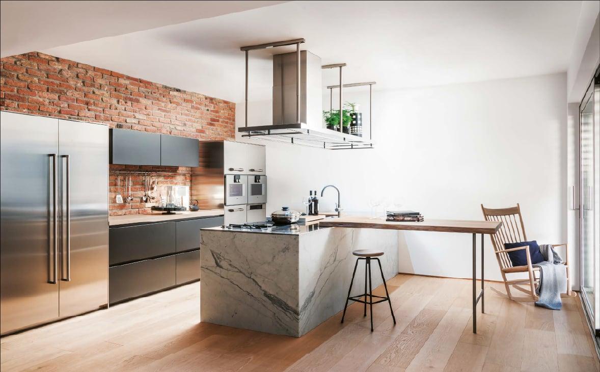 Kitchen with a marble-effect island and bar stools under a hanging shelf, a brick wall behind