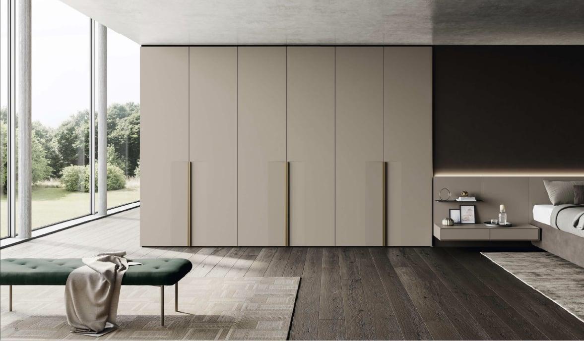 Wall of pale handleless wardrobes with full-height pulls beside a garden window, a green bench in front