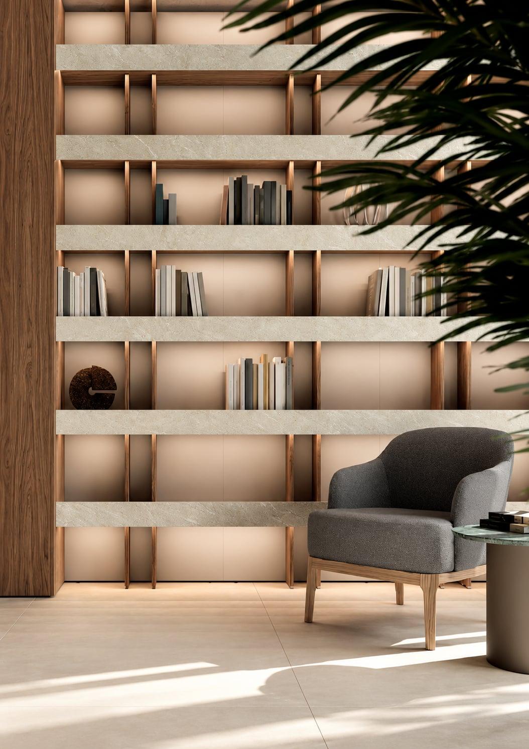 Wall of lit open shelves in warm wood, a grey armchair and a palm in front
