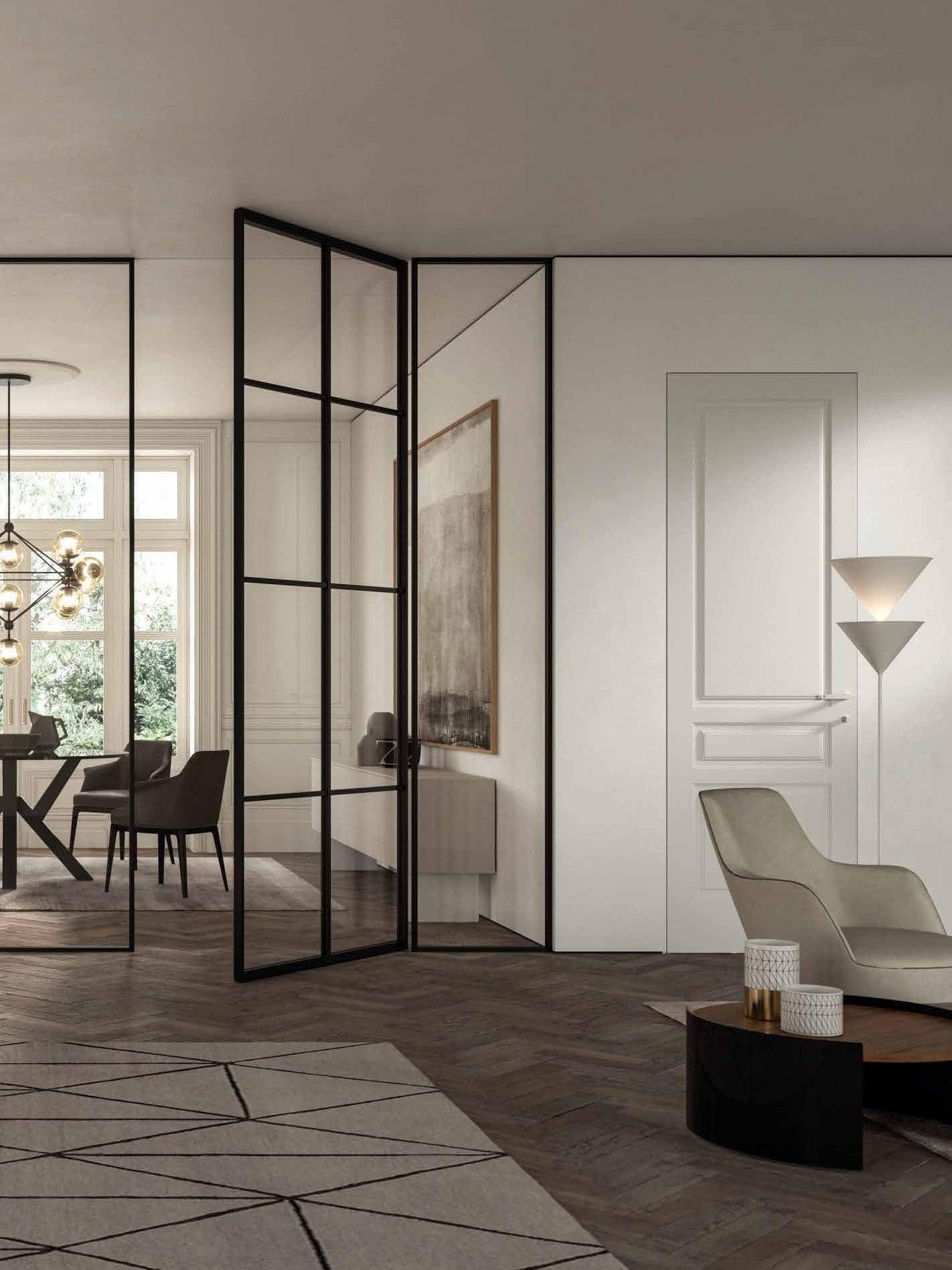Black-framed glass partition doors opening onto a dining room with a chandelier and herringbone parquet