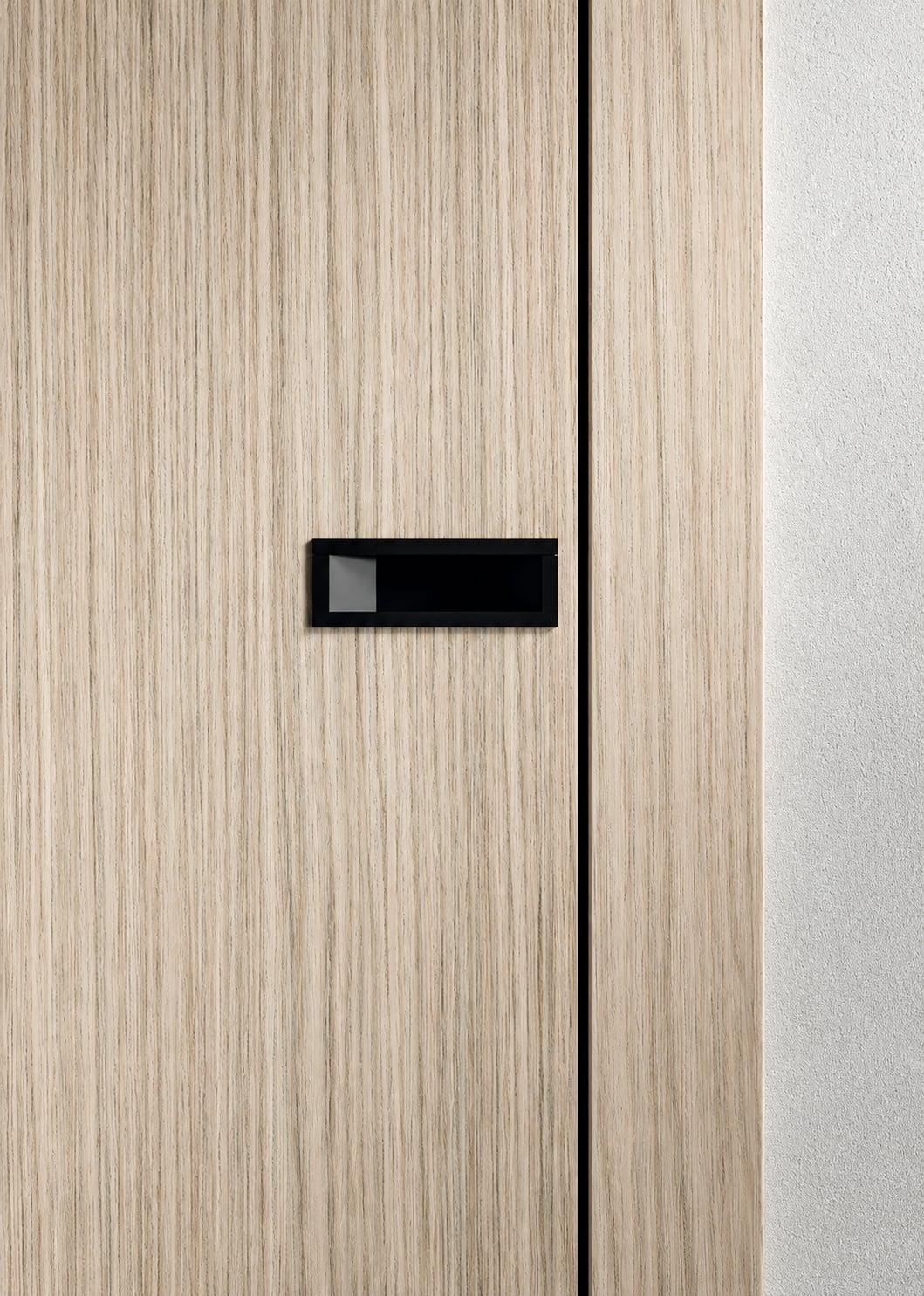 Close-up of a pale wood door with a black flush handle beside a metal panel