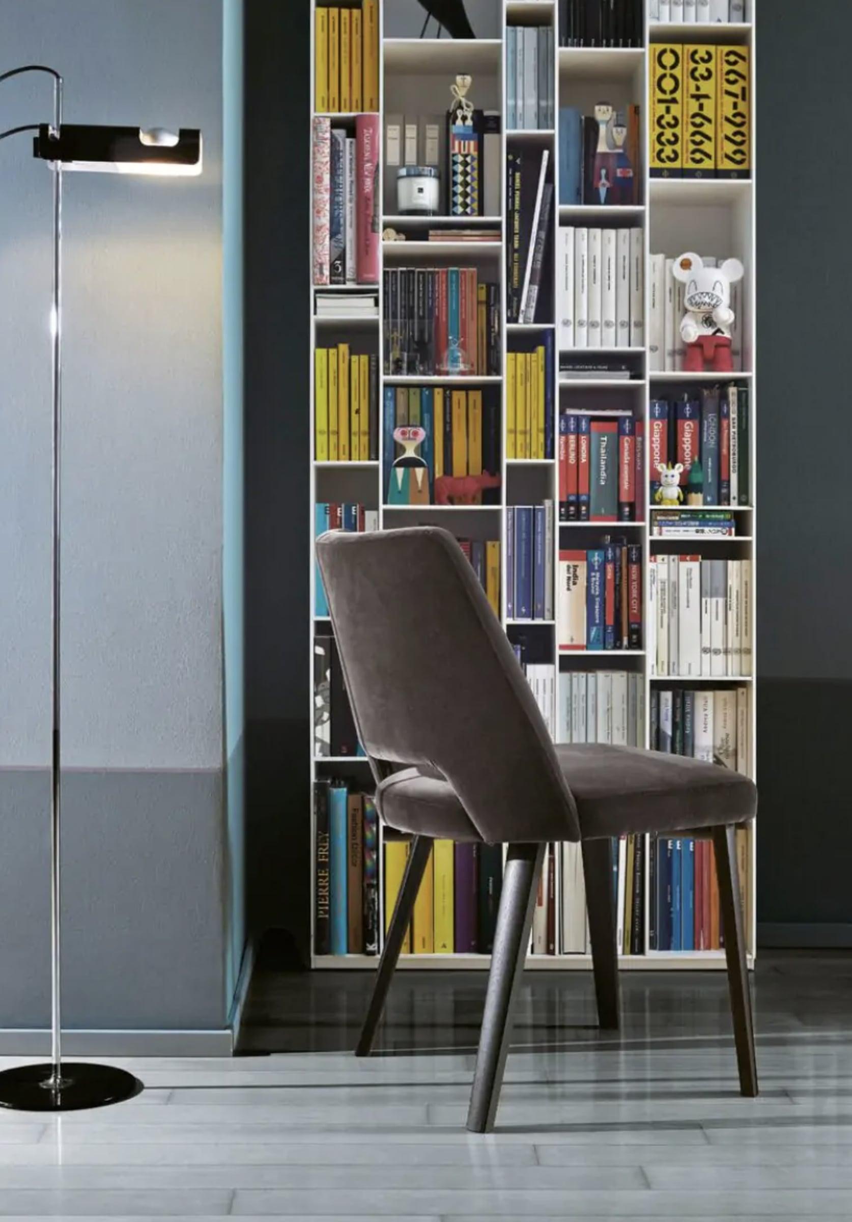 Upholstered chair in front of a colourful bookcase with a floor lamp