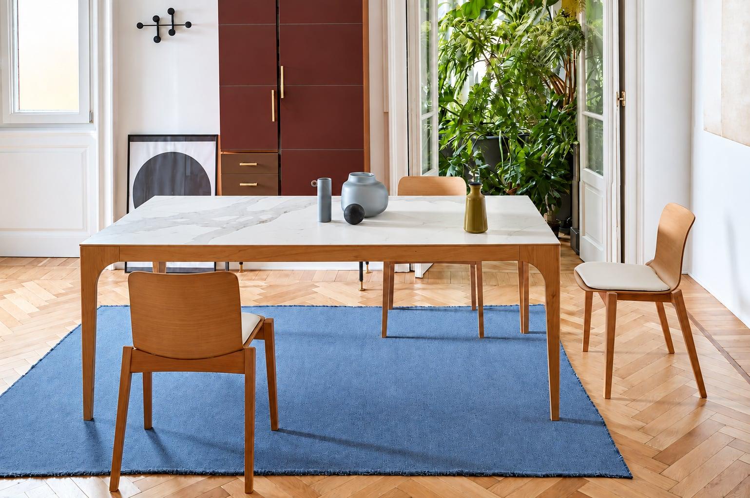 Pale wood dining table and chairs on a blue rug by a window