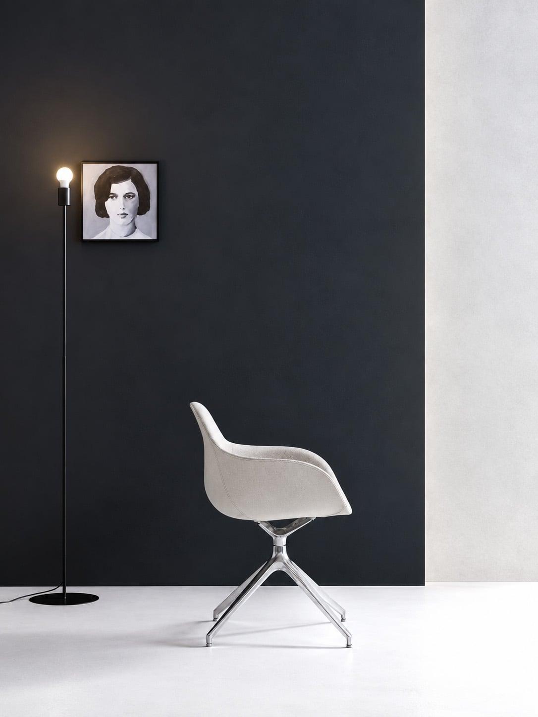 White shell chair on a chrome base in front of a dark wall