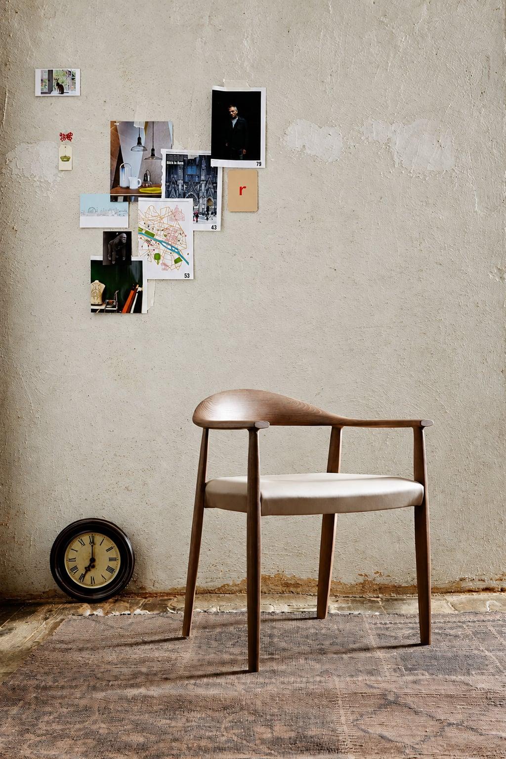 Walnut armchair with a pale seat against a plaster wall