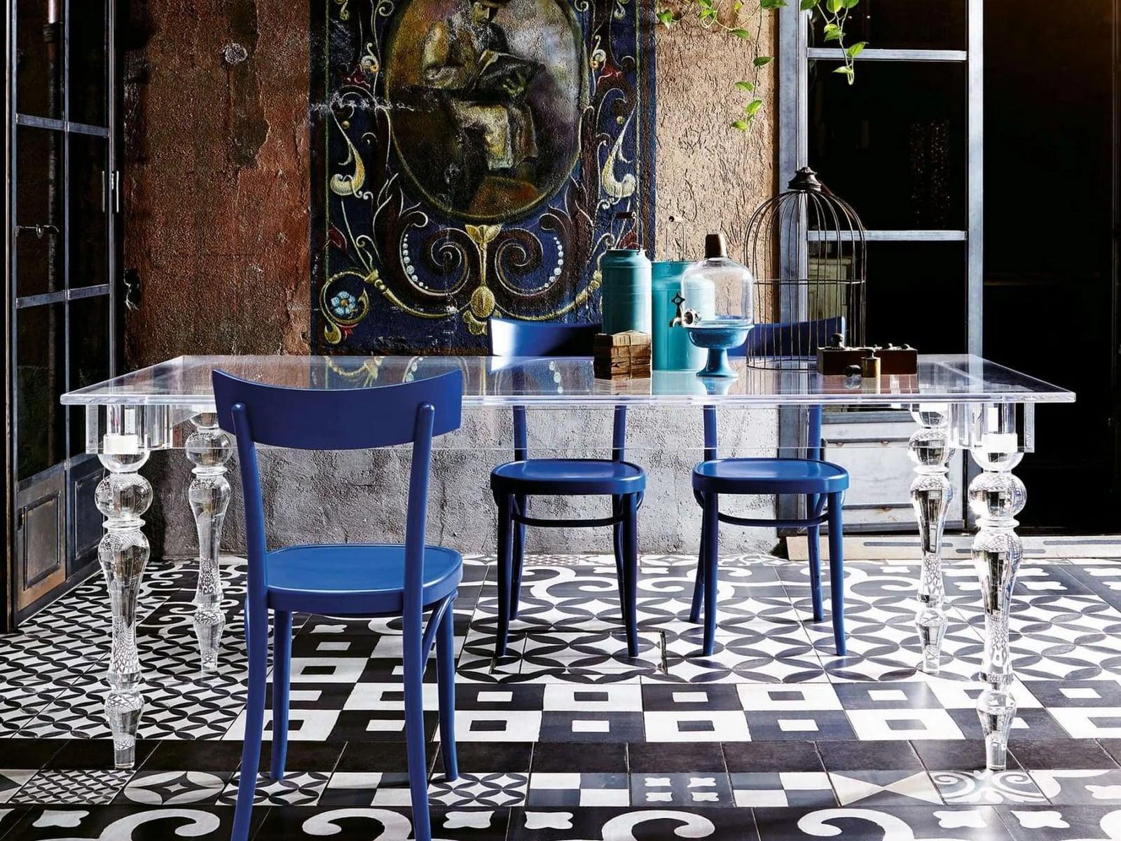 Glass dining table with blue chairs on a patterned tile floor