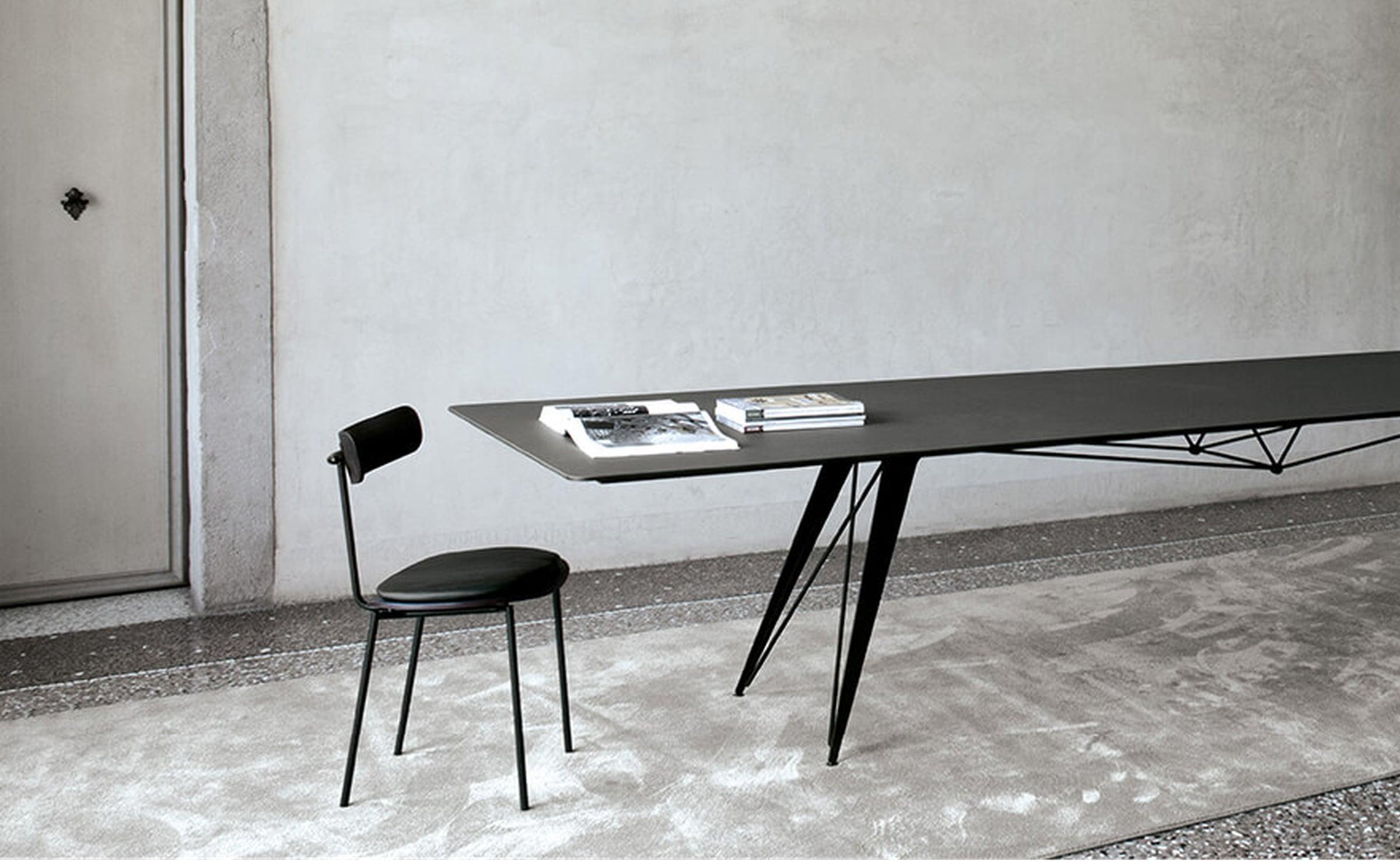 Black dining table on splayed legs with a black chair in a concrete room