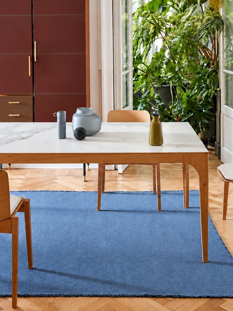 Pale wood dining table and chairs on a blue rug by a window