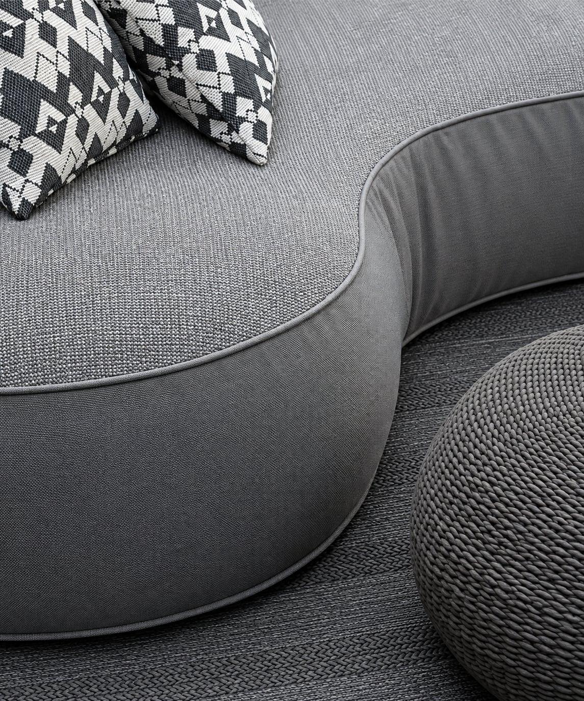 Close-up of a grey outdoor sofa with patterned cushions and a woven pouf