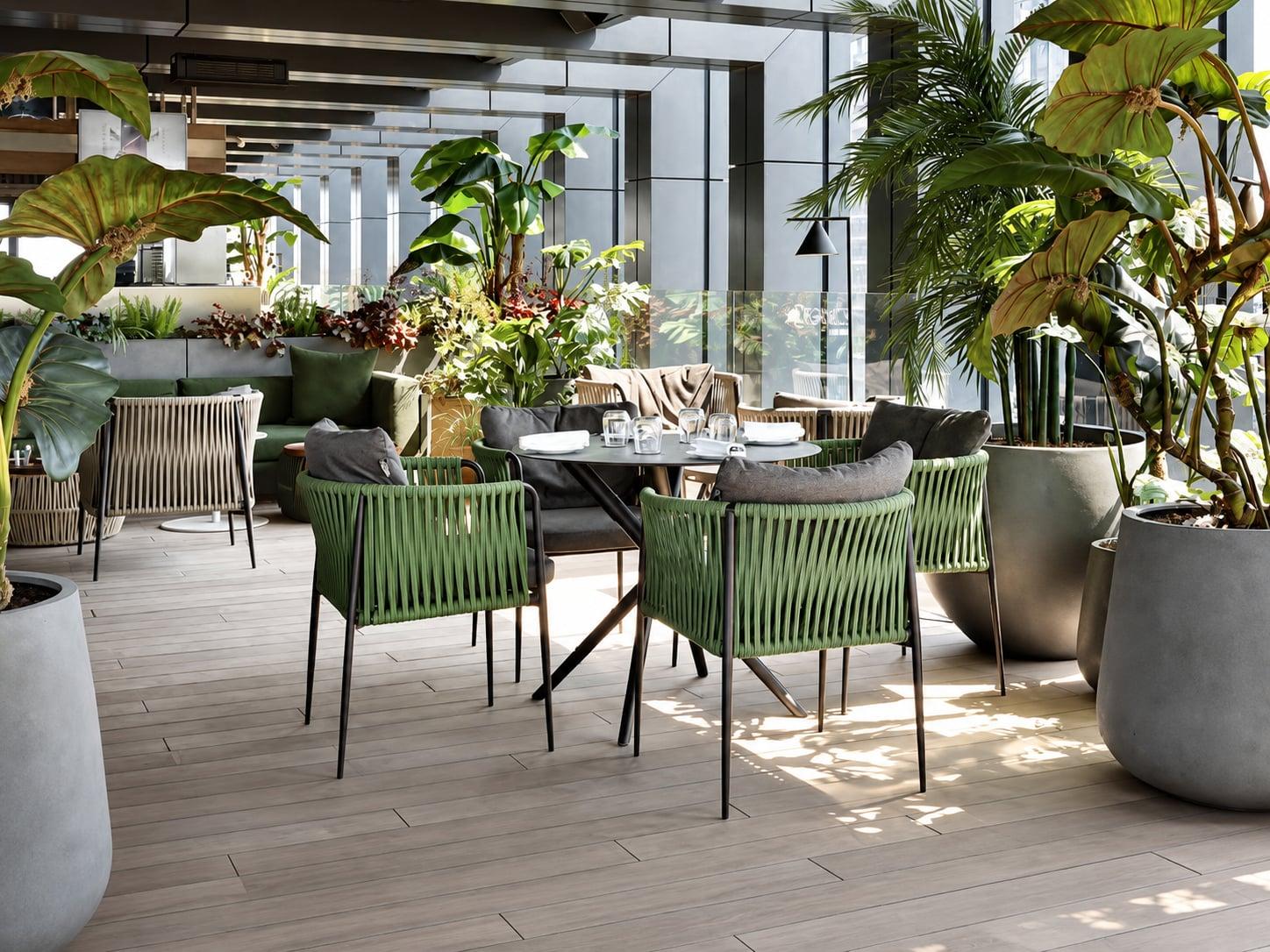 Covered terrace with green woven armchairs at dining tables among palms