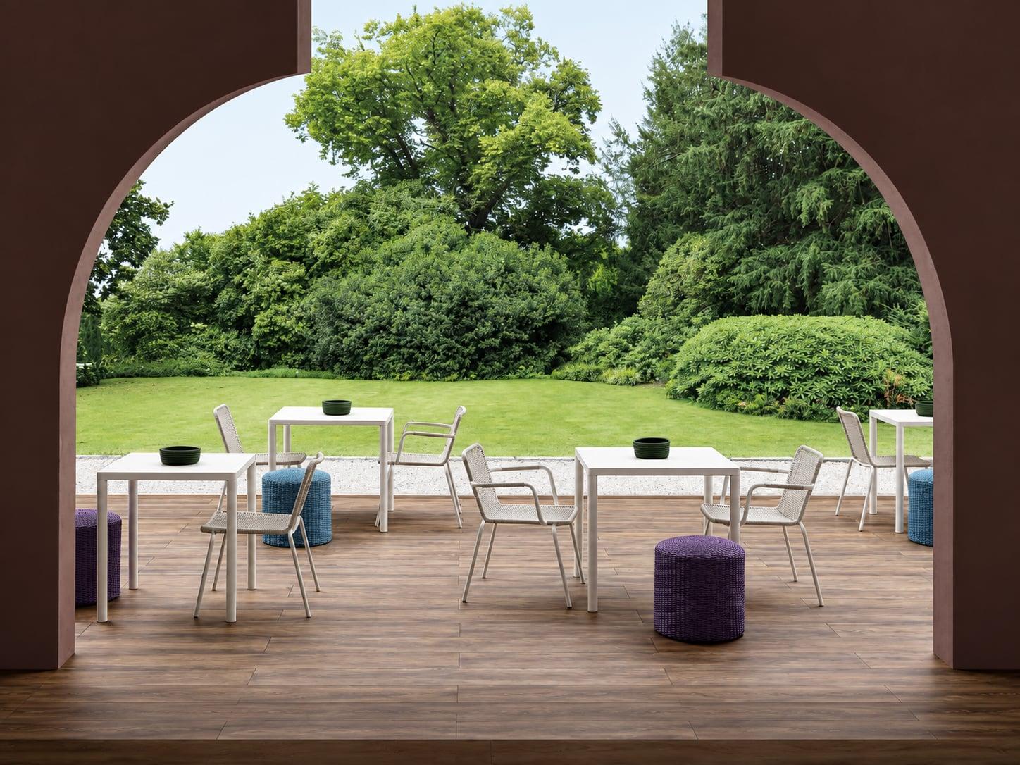 Outdoor dining tables and chairs on a deck, seen through a dark arch onto a lawn