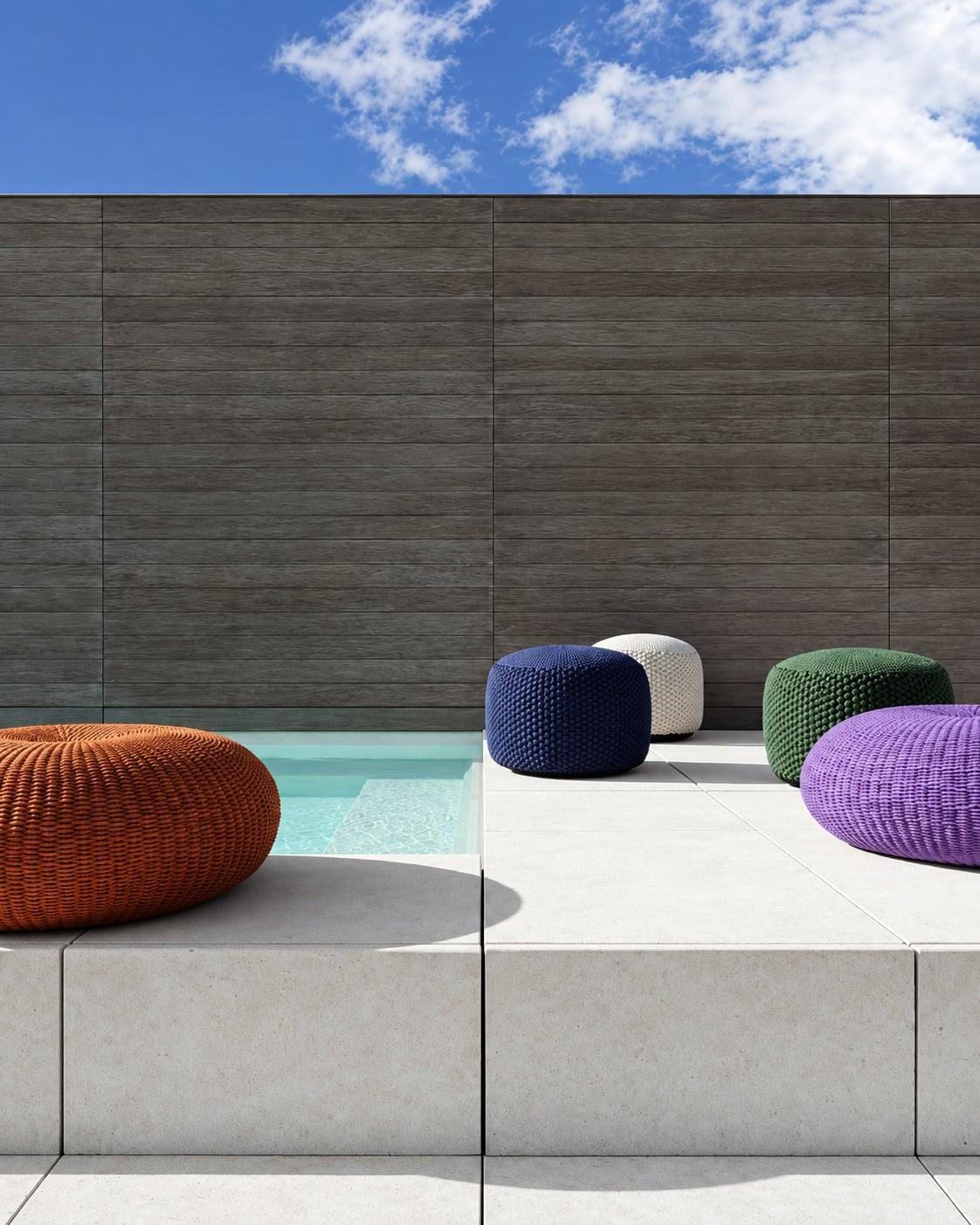 Orange, green and purple woven poufs on a stone terrace by a pool