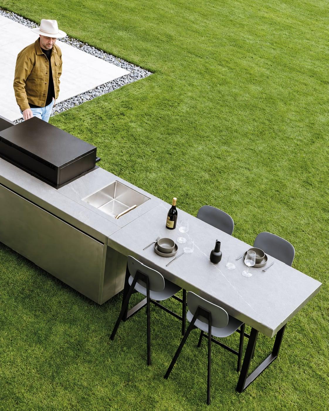 Green outdoor kitchen island with a white top and stools on a lawn, seen from above