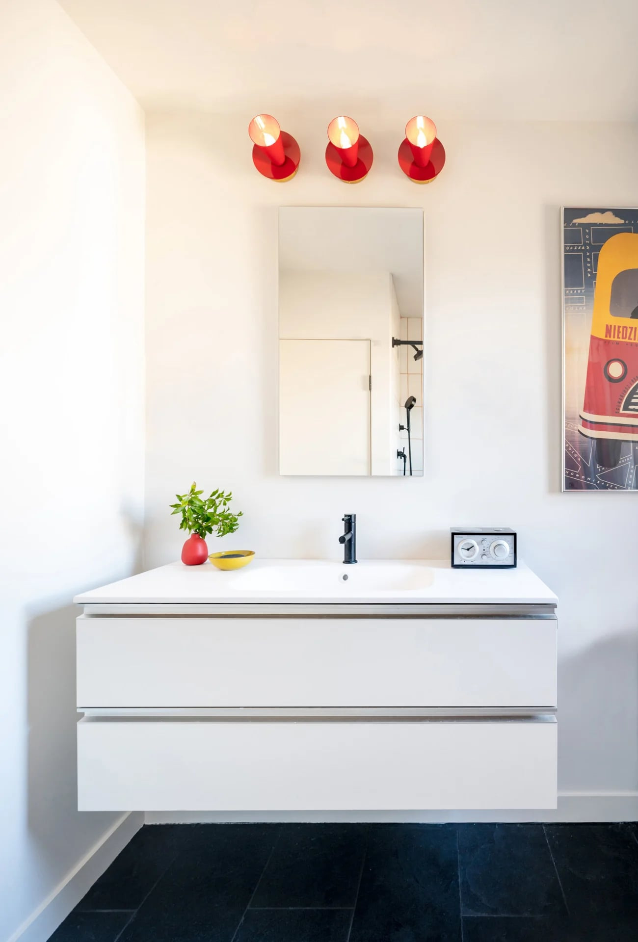 White vanity under a mirror with three red pendant lights