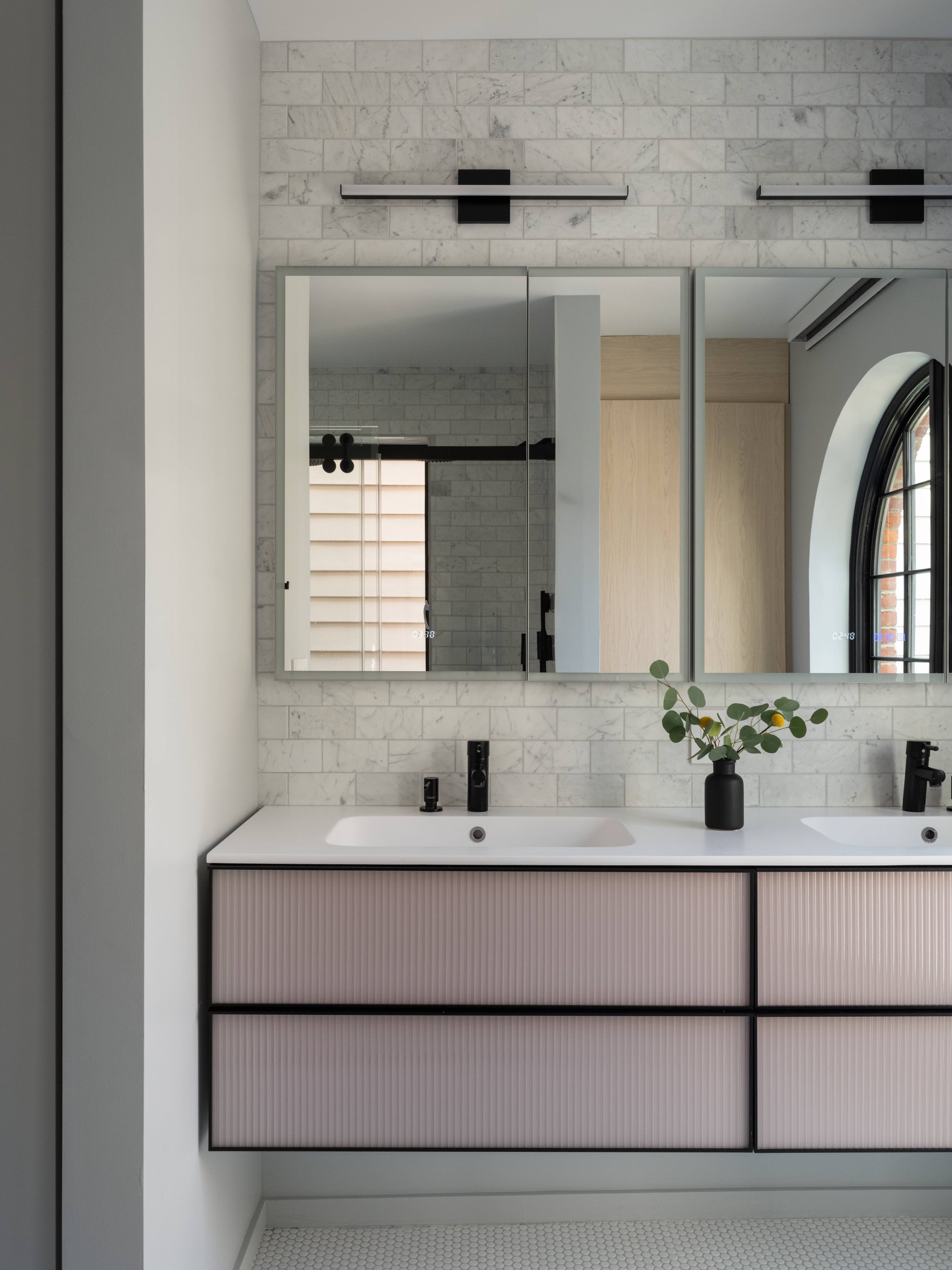 Double vanity with reeded pink drawers and a black frame under a wide mirror, on a white brick-tiled wall