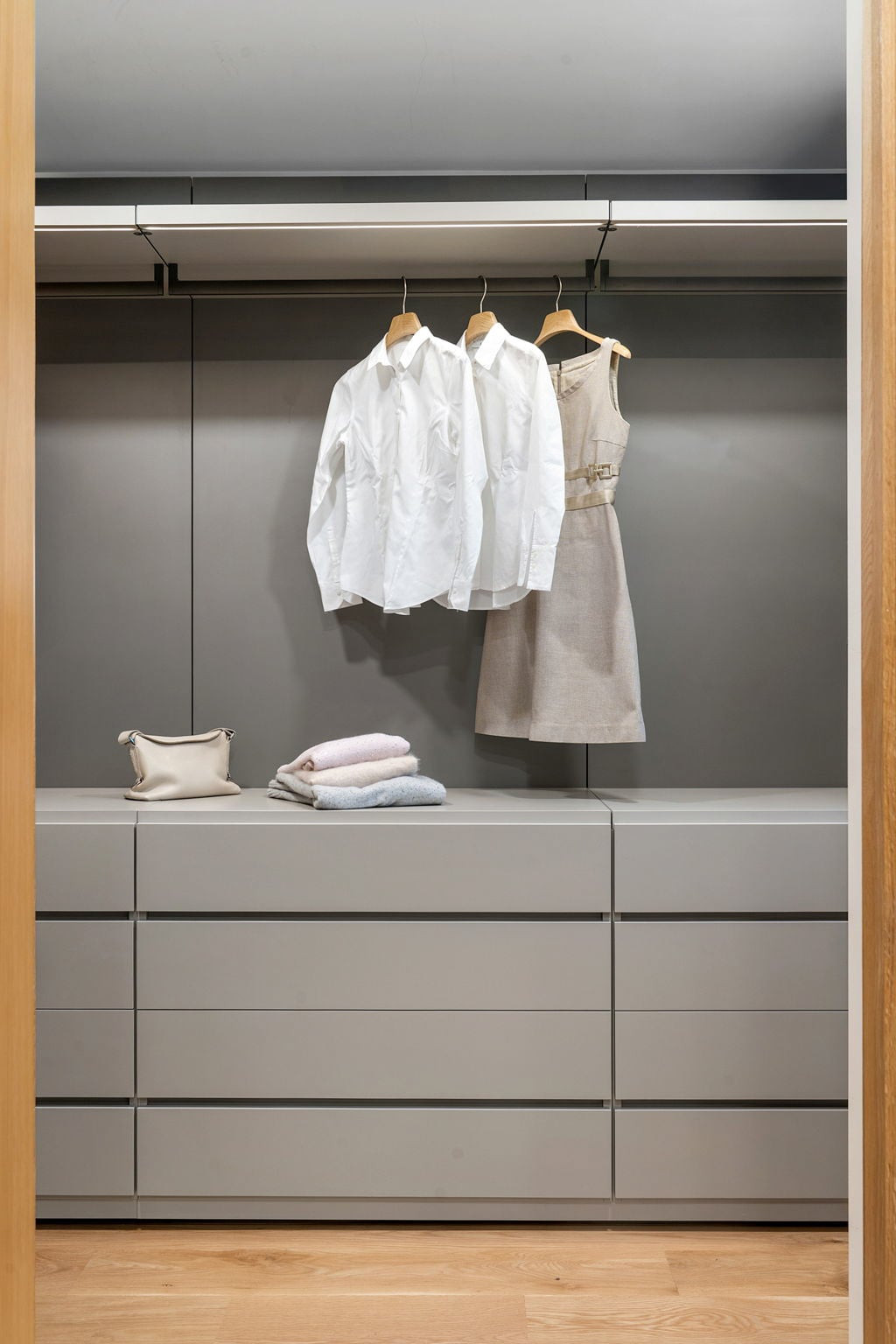 Open wardrobe in grey lacquer with hanging shirts over a chest of drawers, framed in oak