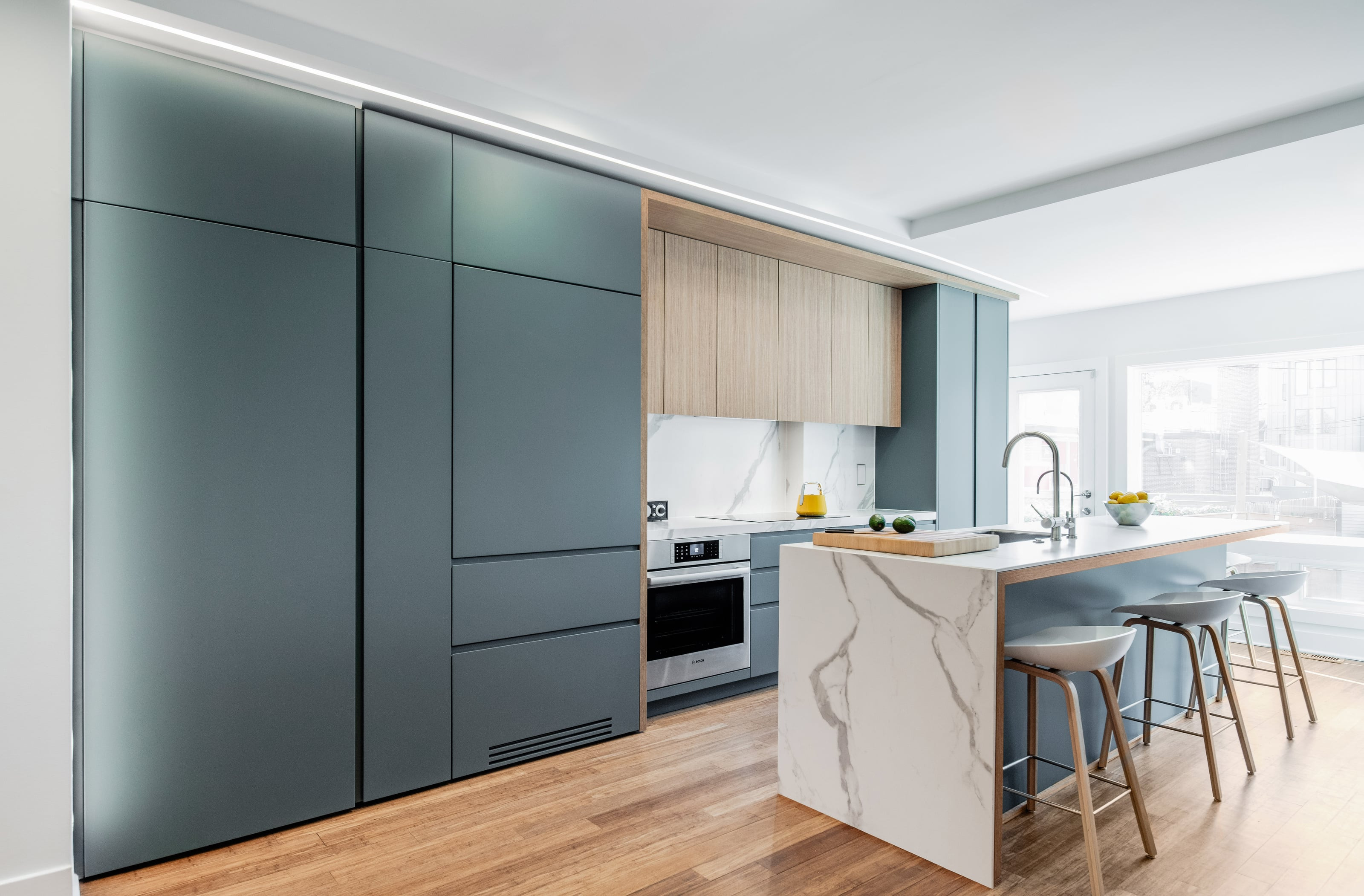 Kitchen with teal full-height cabinets, oak wall units and a white marble waterfall island with stools